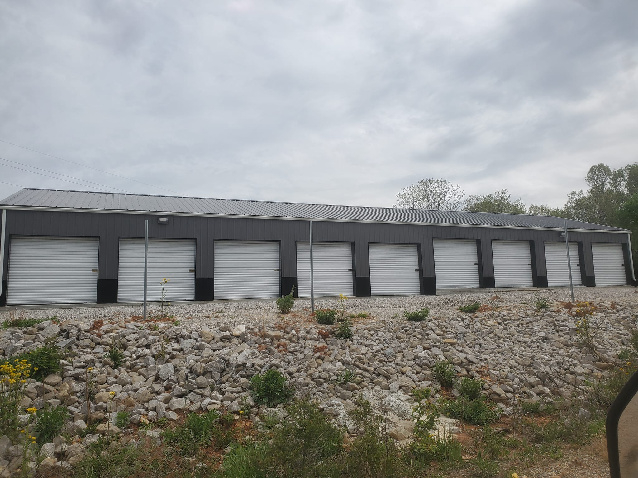 A fenced in storage unit building with 9 units each having an overhead door.